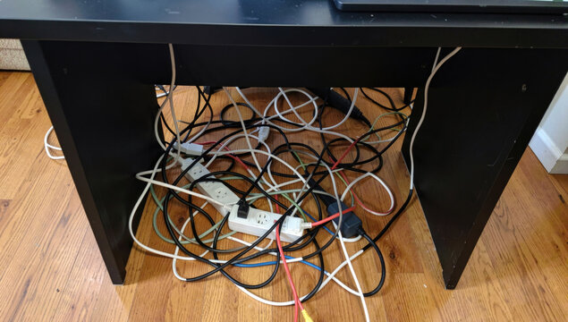 A cluttered computer desk with tangled wires and cords