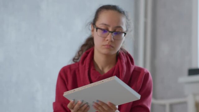 Asian Woman Inspects Panel Placement. Young Woman Ensures Proper Panel Alignment Quietly Indoors. Asian Woman Meticulously Examines Panel Positioning And Borders Prior To Securing Parts Indoors