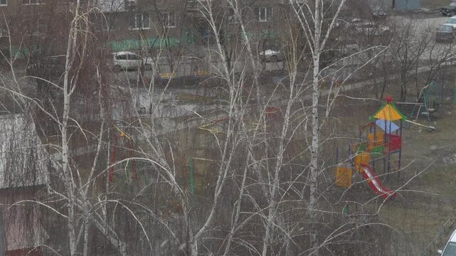 Gloomy playground view through bare birch branches, dull overcast sky