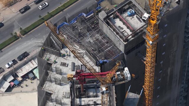 Aerial view of tower crane lifting material at skyscraper construction site