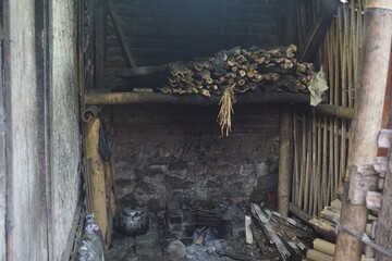 Fototapeta premium Rustic bamboo cooking area with brick hearth, pots, firewood, and bamboo shelves in a traditional rural setting.