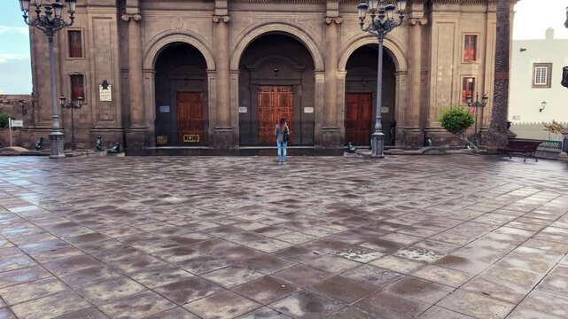 Woman walking towards the historic Las Palmas Cathedral on a cloudy day in Gran Canaria, Spain, visiting a landmark