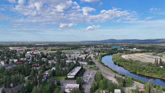 Stunning aerial panorama revealing the city of fairbanks, alaska, with the beautiful chena river flowing alongside lush green forests under a partly cloudy summer sky in the united states
