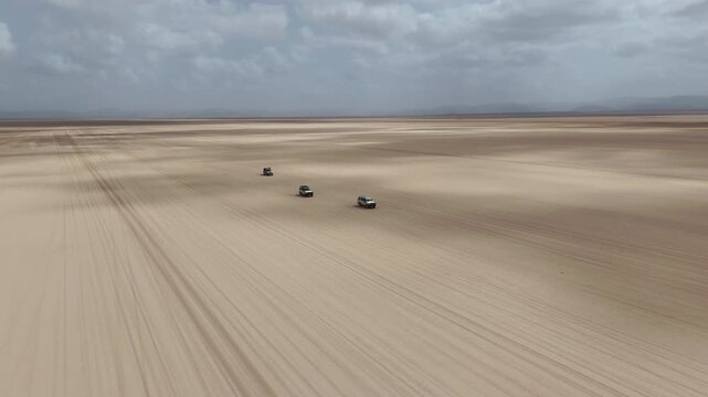 Aerial footage of vehicle traveling through harsh desert environment with dust, wide revealing drone shot. Djibouti Africa.