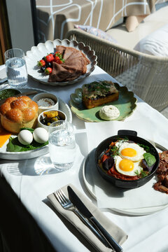 Full breakfast table with eggs, pancakes, sandwich and porridge. Breakfast includes fried eggs in a pan, chocolate crepes with berries, an open ham sandwich, and a bread platter with dips