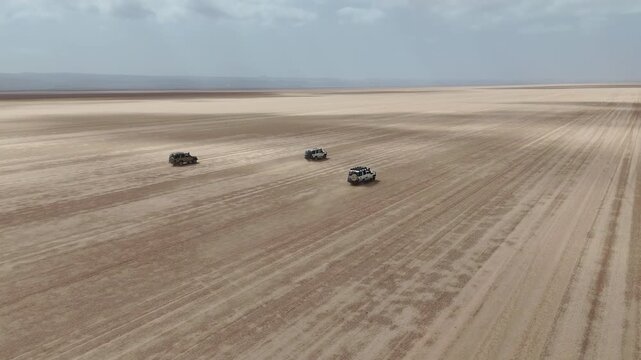 Drone footage of vehicles driving through vast desert landscape with rugged terrain and dust trails. Djibouti Africa.