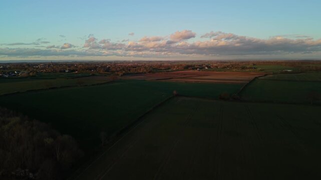 Aerial few of green farmers fields in North Yorkshire town at sunset with orange glow and shadows crossing the large flat fields