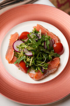 Fresh Salmon Salad with Cherry Tomatoes and Radish. Close-up of a gourmet salad featuring salted salmon slices, fresh mixed greens, cherry tomatoes, and radish on a pink plate