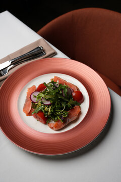 Fresh Salmon Salad with Cherry Tomatoes and Radish. Close-up of a gourmet salad featuring salted salmon slices, fresh mixed greens, cherry tomatoes, and radish on a pink plate