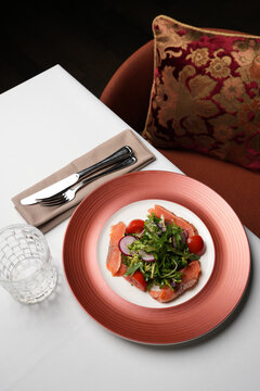 Fresh Salmon Salad with Cherry Tomatoes and Radish. Close-up of a gourmet salad featuring salted salmon slices, fresh mixed greens, cherry tomatoes, and radish on a pink plate