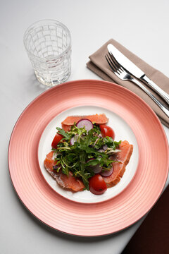 Fresh Salmon Salad with Cherry Tomatoes and Radish. Close-up of a gourmet salad featuring salted salmon slices, fresh mixed greens, cherry tomatoes, and radish on a pink plate