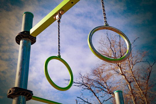 Anillas de calistenia al aire libre que simbolizan fuerza, disciplina, cultura del fitness urbano y entrenamiento funcional con peso corporal. Anillas met&aacute;licas de gimnasia colgando de cadenas