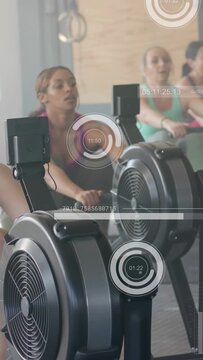 Vertical video: Front erg starting fitness class by monitor as women rowing HUD dials tracking pace