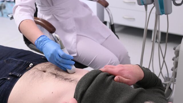 A doctor performs an ultrasound of the abdominal cavity of a male patient lying on a couch.
