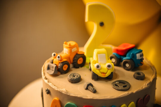 Cute construction themed birthday cake for a 2-year-old with toy tractors, trucks, and edible bolts. Creative dessert for a boy's party with a yellow number two topper.