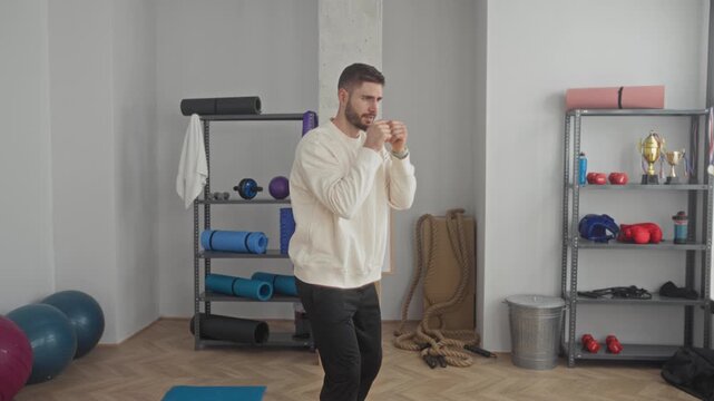 Man shadowboxes with fists in a fitness studio, throwing jabs and working footwork among mats and ropes; training determination.