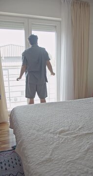 A young man begins his day with a gentle morning stretch, opening the window to let in fresh air. This serene moment captures a healthy start to the day, promoting wellbeing and a positive lifestyle.
