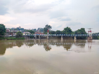 Fototapeta premium Bridge of Katulampa Dam in Bogor, supported by concrete pillars with blue railing, busy with motorcycle traffic crossing over calm reflective river water