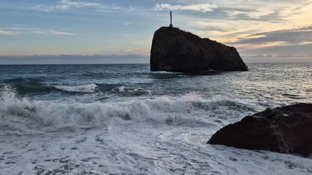 Ocean waves sunset, powerful sea crashes on rocky beach, tranquil landscape with a cross on an island at golden hour