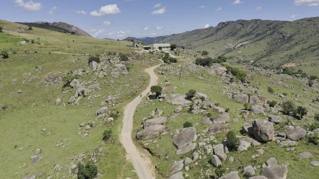 Drone lowers over hiking trail and two hikers climb the hill on a sunny day at Sibebe Rock near Mbabane, Eswatini