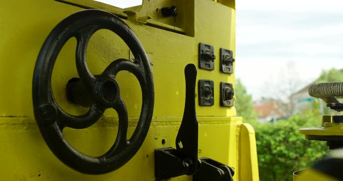Close up of a black handwheel and levers on a yellow industrial machine or locomotive control panel