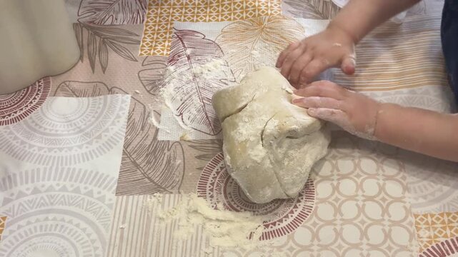 A child in a blue shirt kneads dough with an adult on a patterned table, learning to bake, joyful family moment, cozy lifestyle.