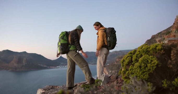 Friends, hiking and high five on mountain with hug, sea view or achievement for backpacking trip. Women, embrace and celebration on cliff with ocean scenery, bonding or success for trekking adventure