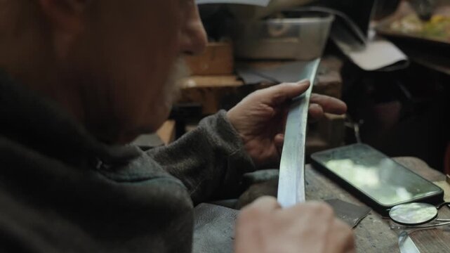 Elderly craftsman working in his old workshop, carefully restoring collectible Japanese bladed weapons