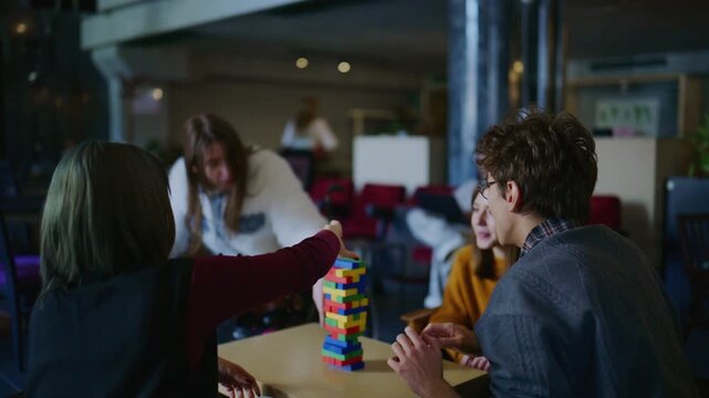 A diverse group of students and friends play a colorful block tower game together. Young people are enjoying a fun, challenging game in a cafe setting.