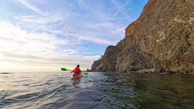 Kayak sunset ocean man paddling orange boat near rocky cliffs during a peaceful summer evening adventure at sea
