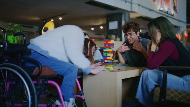 A diverse group of students, including one in a wheelchair, engages in a block-stacking game. Young friends focus intently on the colorful tower, enjoying their inclusive playtime together.