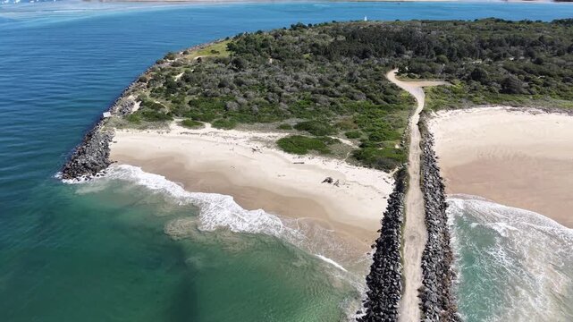 Aerial view of a narrow coastal road curving around a sandy beach and green hills.