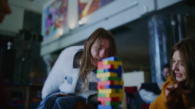 A group of students is focused on playing a challenging tower stacking game at a table. They are engaged in the game, showing concentration and teamwork during their leisure time.