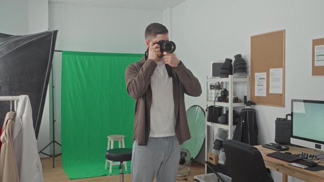 Man holding a dslr camera, checking settings and occasionally raising it to his eye in studio; focused creativity.