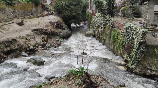 A wide, high-angle shot capturing the powerful flow of the Kakopetria river as it cuts through the rocky landscape of the historic mountain village in the Troodos region of Cyprus.