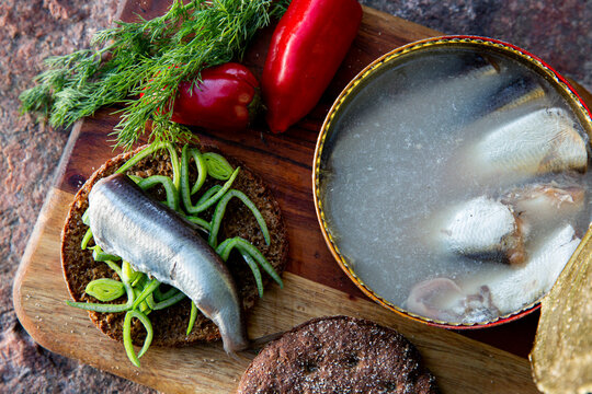 Open tin of Swedish surstromming fermented herring, traditional sandwich with rye bread, dill and peppers on rustic board, extreme food concept
