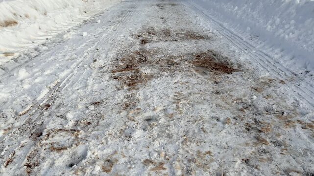 Snow cleared pedestrian path alongside highway, showing salted and grit strewn surface, high plow berm, tire tracks and compacted.