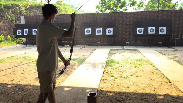 Young man preparing bow and arrow at outdoor archery range, practice session before shooting, focus and concentration in target sport, active leisure activity.