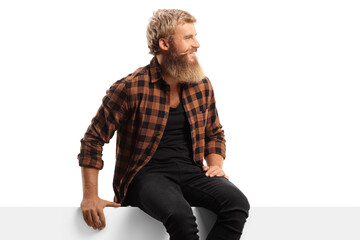 Obraz premium Young bearded man sitting on a white panel board and looking to the side
