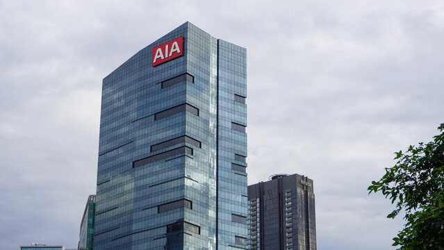 An editorial shot of the AIA Central building, a prominent glass-clad skyscraper located in the heart of Jakarta's financial district. The image highlights the sleek architectural design.