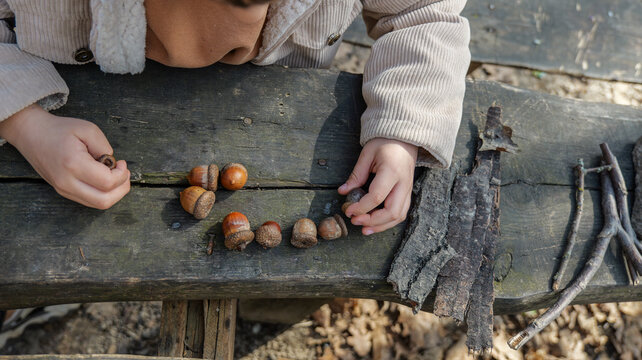 Child's hands arranging acorns and bark on a rustic wooden surface outdoors