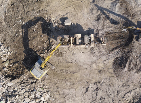 Aerial view of an excavator loading construction debris into a crusher, processing rubble and soil on a dusty demolition recycling site. New Taipei, New Taipei City, Taiwan.