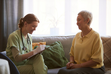 Fototapeta premium Senior woman meeting female nurse, discussing care plan and answering questions during nursing home visit