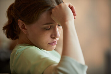 Obraz premium Close up of young adult Caucasian female caregiver resting head on hand, showing stress and fatigue in nursing home