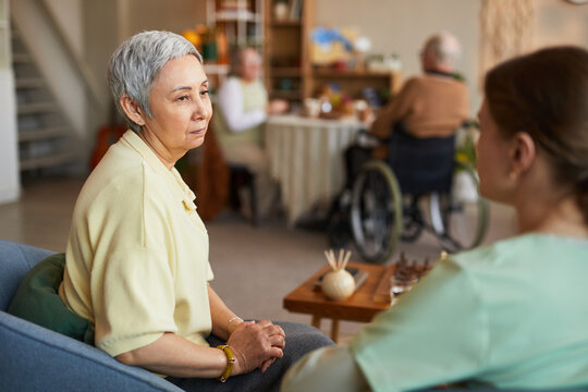 Senior Asian woman receiving support from female caregiver in nursing home, discussing care needs and assisted living services