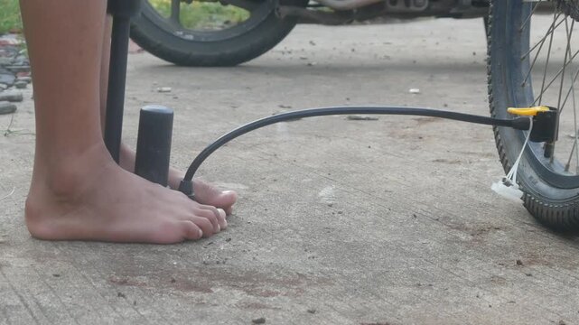 A man's feet holding the base of a manual hand pump while pumping up a bicycle tire outdoors