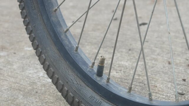 A person is pumping up a bicycle tire using a manual hand pump outdoors.