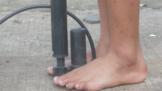 A man's feet holding the base of a manual hand pump while pumping up a bicycle tire outdoors