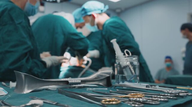 Surgical tools arranged on a sterile table while medical team surgeons operating in the background. Medical equipment, preparation and teamwork in surgery 