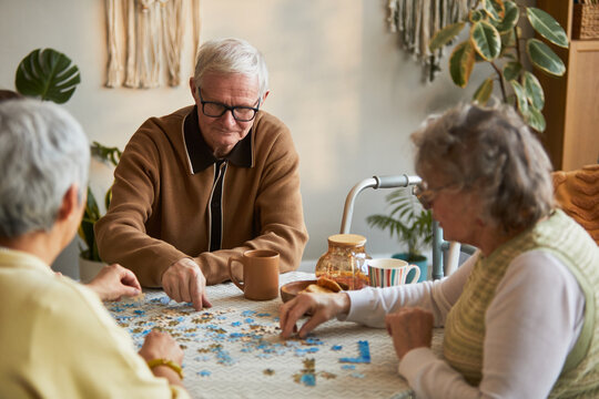 Senior man and senior women assembling jigsaw puzzle in nursing home, supporting cognitive activity and social connection